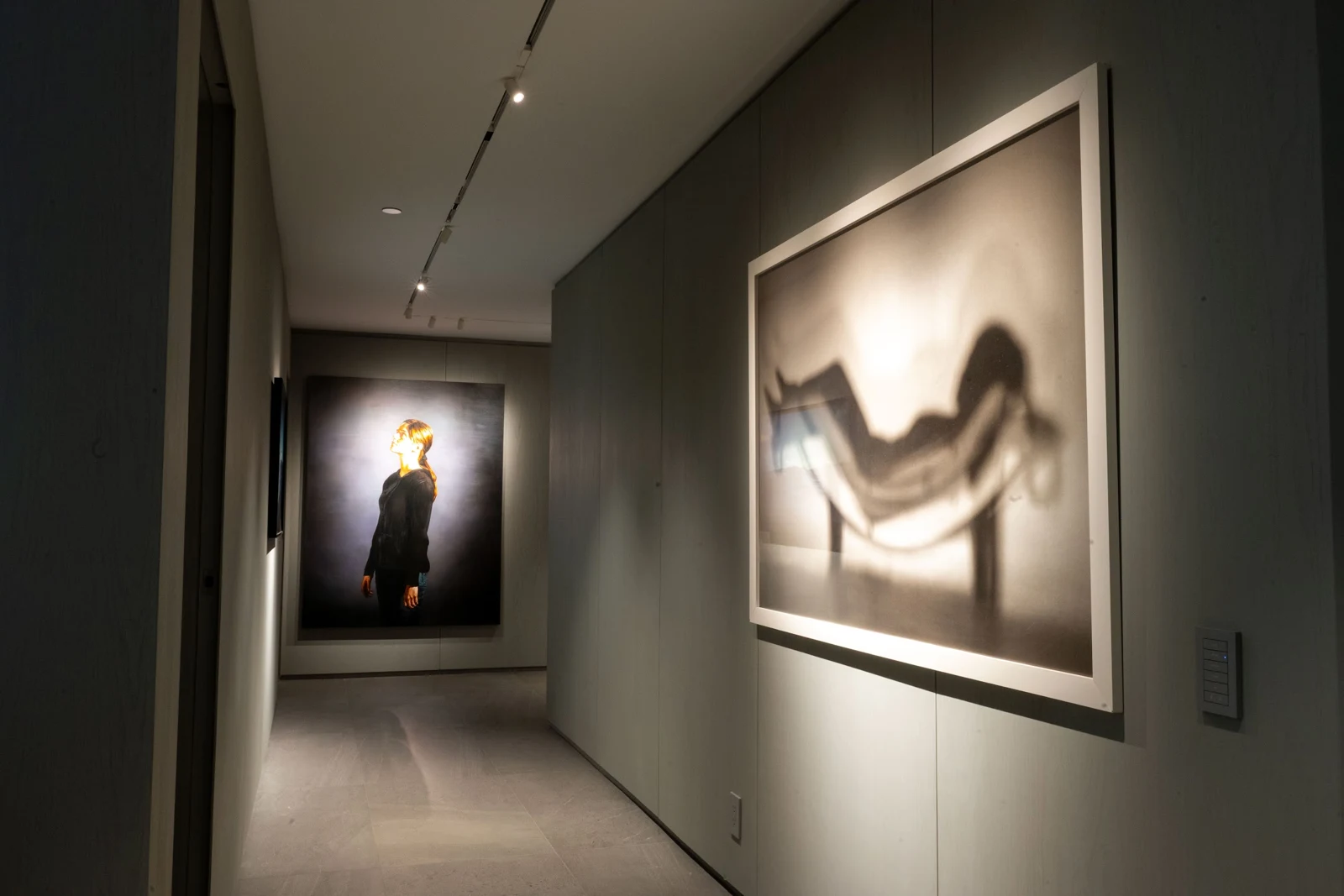 Track-mounted spotlights illuminating framed artwork along an apartment hallway